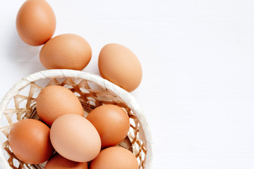 Brown chicken eggs in a straw basket on white wooden background. Top view with copy space.