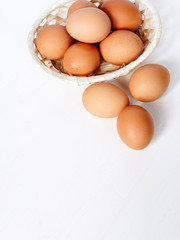Brown chicken eggs in a straw basket on white wooden background. Top view with copy space.