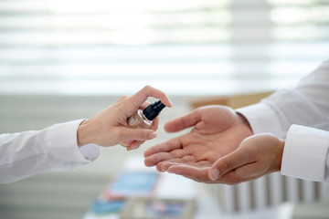 Female hand holding a sanitizer and spraying it on mans hand