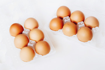 Brown chicken eggs in plastic container on white wooden background.