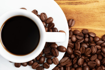 A cup of coffee, a saucer, and scattered grains on the wooden table.