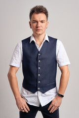Portrait of trendy man in white shirt and vest posing over gray background
