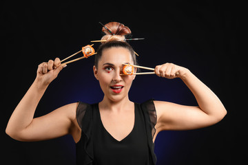 Beautiful woman with tasty sushi on dark background