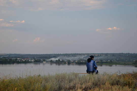 lonely woman sitting on a bench and relaxing by evening lake and sudown clouds