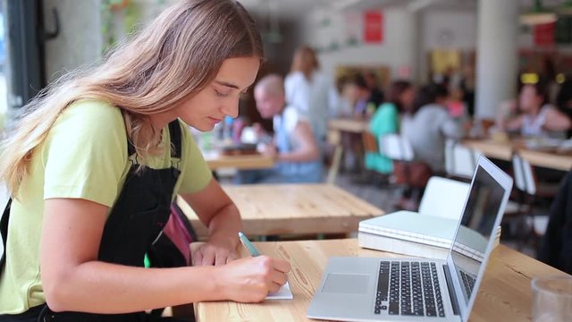 side portrait female writes in notebook. concentrated young beautiful white fwoman writes notes study distance or work as freelancer. pretty girl works remotely in coffee shop, hard working goals