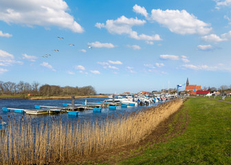 The small boat marina in the village of Schaprode on the German island of Rügen in the Baltic Sea. In the foreground is reed and in the background the small village with a church. 