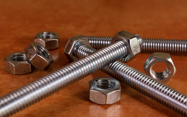 Some screws and nuts lie criss-cross on top of each other on a red-brown tile. A macro shot in the...