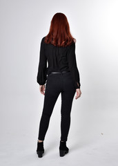 Portrait of a pretty girl with red hair wearing black jeans, boots and a blouse.  full length...