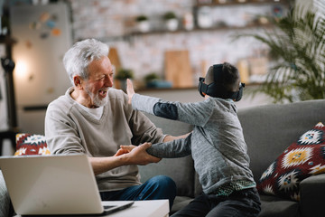 Grandson and his grandpa playing with VR at home on sofa. Grandfather and a little boy having fun at home.	
