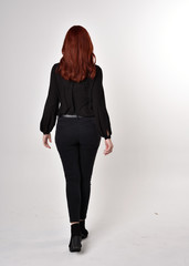Portrait of a pretty girl with red hair wearing black jeans, boots and a blouse.  full length...