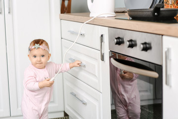 Little baby playing with electric plug in kitchen. Child in danger