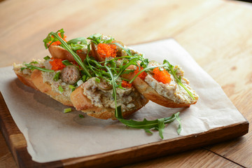 Italian bruschetta with salmon butter, capelin caviar, cherry tomatoes and parsley served on wooden cutting board