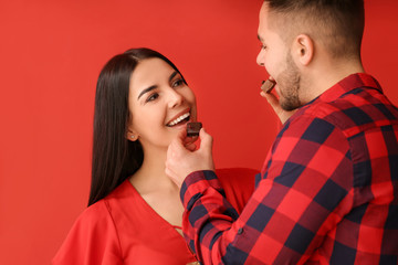 Beautiful young couple with tasty chocolate on color background