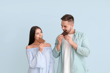 Beautiful young couple with tasty chocolate on light background