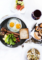 American Breakfast with sunnyside eggs, beans and sausage, on a table with granola, fruits and pastry, from the above