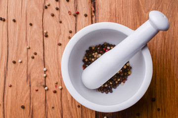 White mortar and pestle with pepper and spices mix on rustic wooden table.