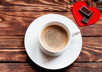 cap of coffee with foam, two chocolates on red heart on the wooden table.  Flat Lay with no people