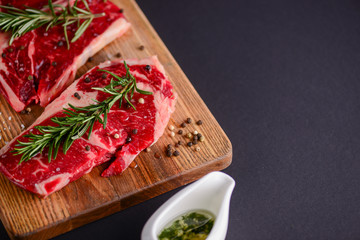 Fresh raw steak on wooden cutting board over black background with spices, top view.