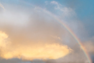 Rainbow against a background of clear, blue sky and golden clouds. Copy Space