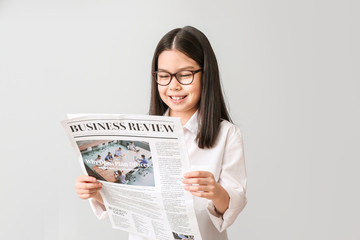 Cute little businesswoman with newspaper on grey background