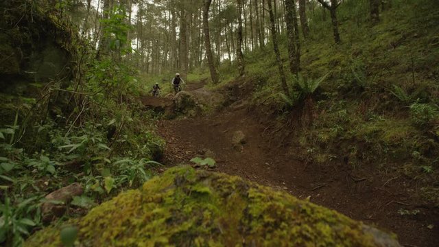 Two professional montain bike riders jumping in the forest in slow motion.