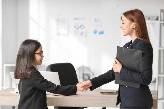 Cute little businesswoman with client shaking hands in office