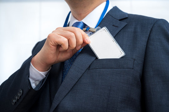 Businessman in suit wearing a blank ID tag or name card on a lanyard at an exhibition or conference.