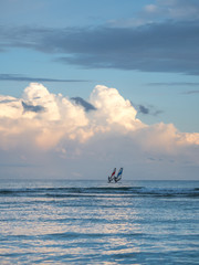 Two windsurfers sailing back with a brilliant cloud above them.