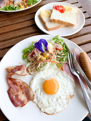 Homemade American Breakfast in Morning, Fried Egg, Ham, Bacon, Sausage and Green Salad on Dish with Side Dish Bread with Jam