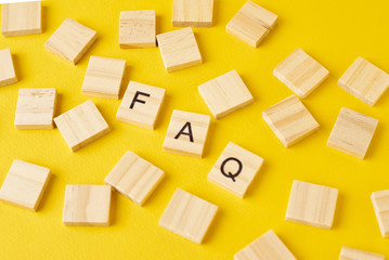 Wooden blocks with abbreviation FAQ on the yellow background, top view. Frequently asked questions...