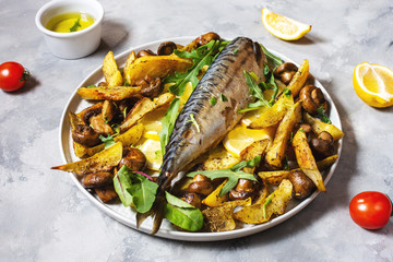 Baked mackerel with lemon, baked potatoes and mushrooms on concrete background.