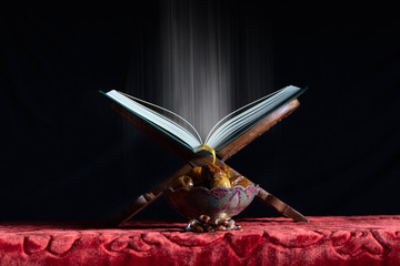 The Holy Quran Allah's holy book with shine and dates on a pot, dark background