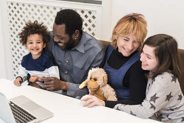 Happy mixed race family, african father, caucasian mother, using computer to make video call in quarantine, modern family using watch multimedia content and surf the internet