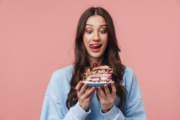 Image of surprised young woman liking her lips while holding cake