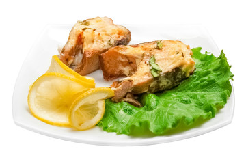 two pieces of fried fish with lemon and green salad leaves on a white background. Isolated object