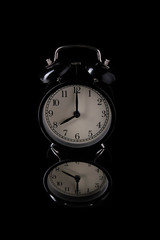 Black alarm clock on a black background with reflection.
