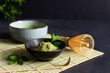 Organic green matcha tea and tea accessories on japanese mat on black background. Japanese tea...