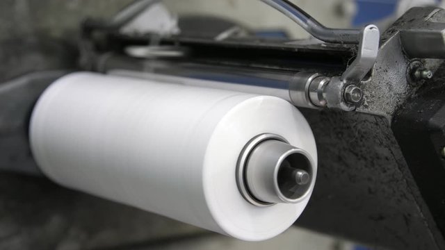 One big coil rotating and getting white string for plastic bags at a machine