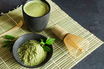 Organic green matcha tea and tea accessories on japanese mat on black background. Japanese tea...
