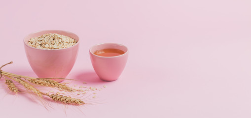 Bowl of dry oat flakes with honey and ears of wheat on light background