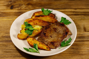 Fried beef steak with potato wedges on wooden table