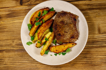 Fried beef steak with potato wedges on wooden table. Top view