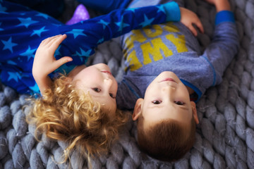 Top view of kids laying in bed with gray cover. Little boy and girl, brother and sister, siblings play on the bed wearing matching pajamas. Family at home. Hugging children in self isolation.