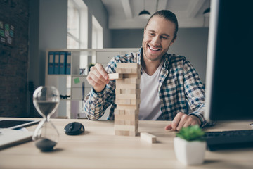 Photo of business guy ignoring working computer monitor lazy secretary playing jenga game building blocks tower toothy smiling excited to win wear casual shirt sit modern office indoors