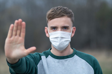 Guy, young man in protective sterile medical mask on his face look at camera outdoors, on asian street show palm, hand, stop no sign. Air pollution, virus, pandemic coronavirus concept. Covid-19