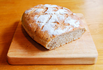 A loaf of home-baked sourdough bread on a wooden chopping board on a wooden table in natural lighting
