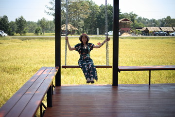 A woman sitting on a swing and a view of the yellow rice field