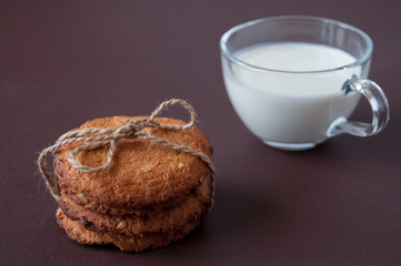 A clear mug of milk and oatmeal cookies tied with string on a brown background
