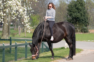 Girl on a pregnant brown horse without a saddle, with white blossom in the background