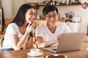 Image of happy couple smiling and using laptop while sitting at table
